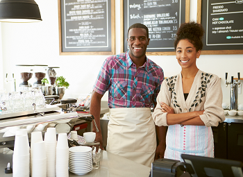 Man and woman small business owners posing in their coffee shop behind the counter