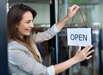 woman small business owner hangs an open sign on storefront